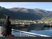 Person tittar från en båt mot Seydisfjördur, Island en vacker sommarmorgon med klarblå himmel.