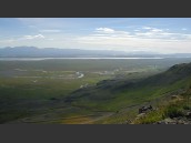 Sommarvy över dalgång med väg 917, en å m.m. på Island. Berg och blå himmel med moln i kulissen.