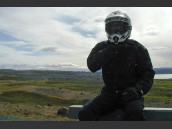 Motorcyklist med hjälmen på sitter på en bänk omgiven av mygg vid Myvatn, Island.