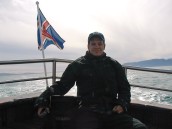 Person sitter i aktern på en båt  ute på havet vid en isländsk flagga.