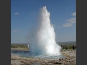 Gejsern Strokkur skjuter upp en vattenpelare mot blå himmel på Island.