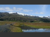 Grusväg och liten bro med berg och glaciär i bakgrunden på Island.