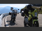 Gul och Grå MC parkerade vid väg på Jaufenpass i Alperna. Körande motorcykel i kurva och höga berg i bakgrunden.