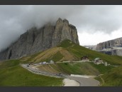 Kurvig väg, bilar och byggnader vid foten av bergstopp i moln i Sella Ronda, Dolomiterna, Alperna på sommaren.