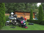 Parkerad MC med öppna väskor och utspridda kläder och prylar på grön gräsmatta och camping i Österrike och Alperna.