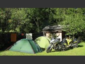 Två uppslagna tält, torklina med handukar och parkerade motorcyklar i Viehofen, Alperna. Grön och lummig skog i bakgrunden.