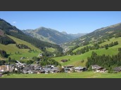 Sommarvy över Saalbach och grön dal i Alperna och Österrike med klarblå himmel i kulissen.