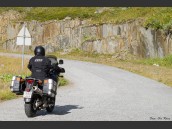 MC med sidoväskor som kör på liten väg med stenklippa vid vägkanten i Beiarn, Nordland, Nordnorge, Norge.