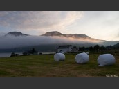 Nyslagen äng med ensilage, dimmoln och berg i vacker solnedgång i Kongsvika, Nordland, Norge.