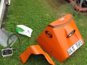 Orange motorhuv med ruta samt ett variatorskydd till Ockelbo 600 på en grön gräsmatta.
